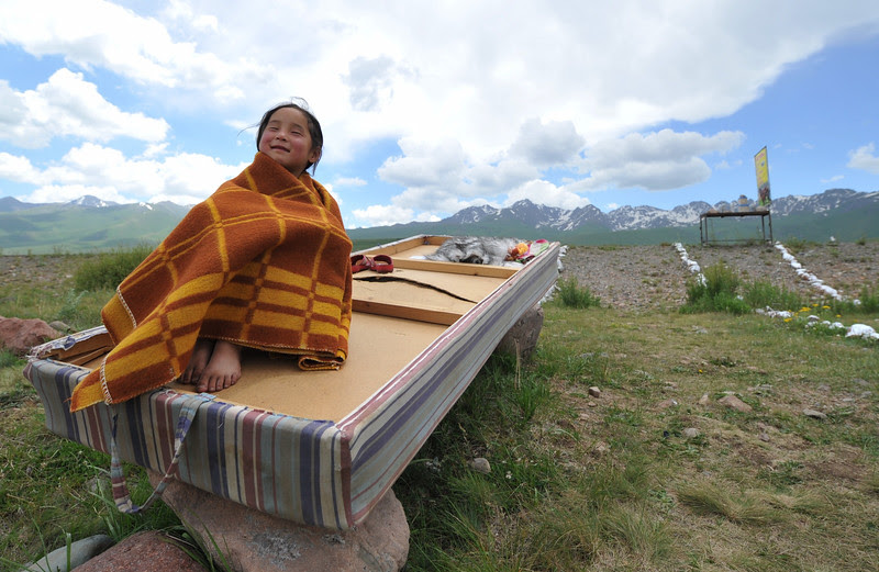 Description of  A little girl sits on a part of the couch at the Suu-Samyr plateau, 2,500 meters above the sea level, near the ancient Silk Road network of trade routes between the East and West, some 200 km outside Bishkek, the capital of Kyrgyzstan, on July 8, 2014. AFP PHOTO / VYACHESLAV OSELEDKO