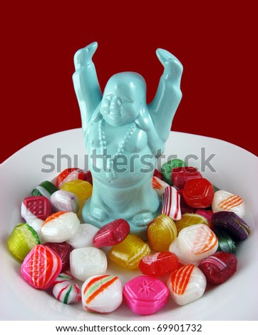 A Tiny Ho Tai Figurine Stands In A Dish Of Brightly Colored Candy ...
