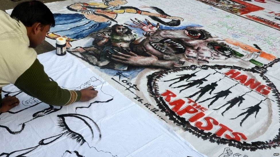 In this photograph taken on December 30, 2012, Indian bystanders write on a banner featuring images of "government and rapists" as it lies on a road in New Delhi, after the cremation ceremony for a gangrape victim.