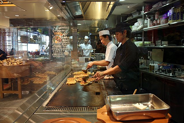 Performance chefs grilling and flipping okonomiyakis and soba