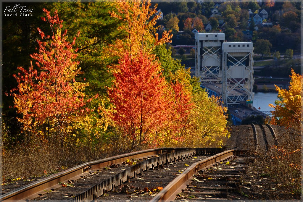 A bright fall color scene with a rail line leading down a hillside, towards the Portage Lake Lift Bridge.