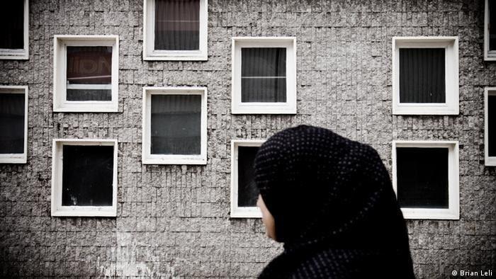 An asylum-seeker wearing a headscarf standing in front of her run-down community home in London 
