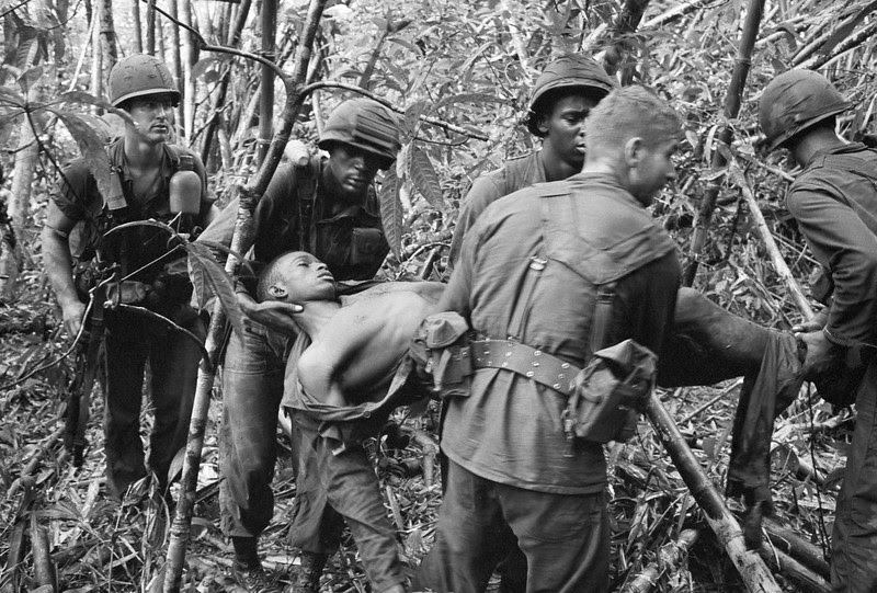 Description of  Soldiers of the 101st Airborne Division carry a wounded buddy through the jungle in May 1966. (AP Photo/Henri Huet)