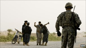 A US soldier looks on as two Afghan police officers frisk civilians - 21 July 2010