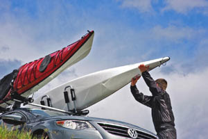 Man loading two kayaks to a vehicle using Thule 835PRO Hullaport PRO Rooftop Kayak Carriers