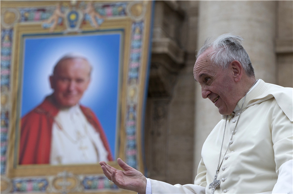 Pope Francis passes by a tapestry depicting late Pope John Paul II as he leaves at the end of his weekly general audience at the Vatican on April 30,...