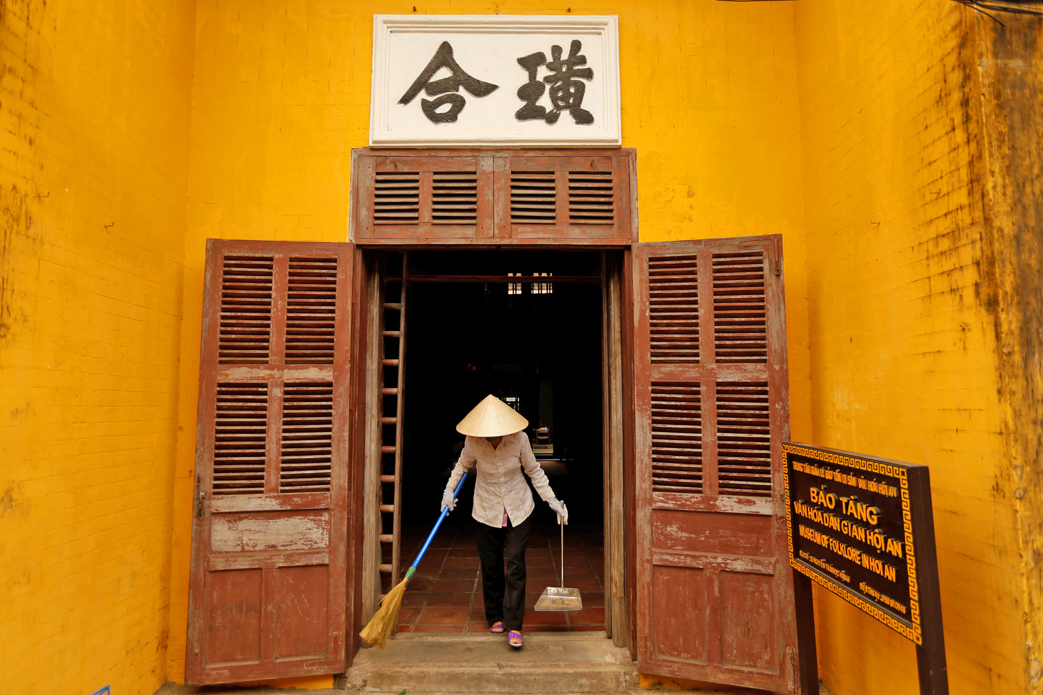 A woman wearing a traditional hat, known as a non la, sweeps an entrance of a museum in Hoi An, Vietnam April 5, 2016. The non la hats are made of readily available materials such as palm leaves, tree bark and bamboo and are visible everywhere in the city, a UNESCO World Heritage site. Hoi An's history as a busy trading port is evident throughout its architecture, a mix of eras and styles, with traditional wooden Vietnamese houses, Chinese temples and French colonial buildings