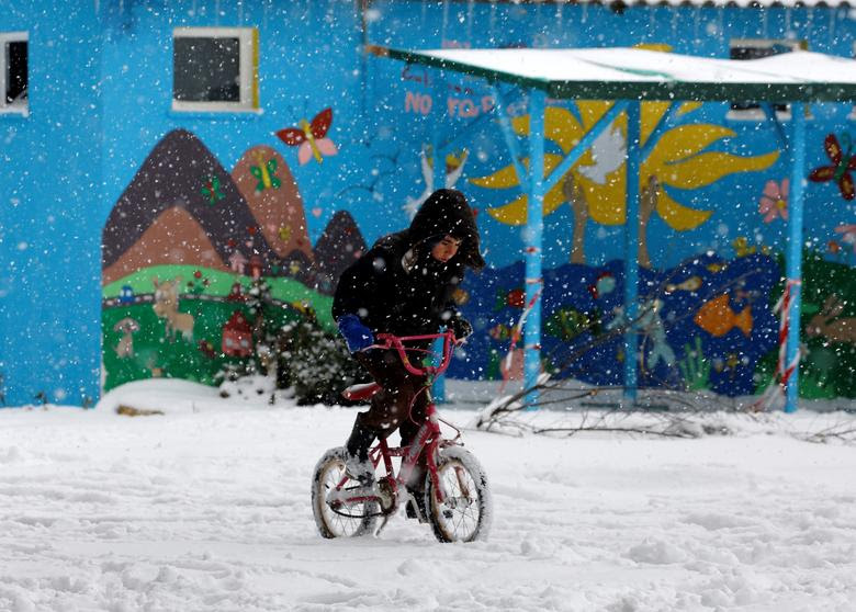 A stranded refugee boy rides his bicycle through a snowstorm at a refugee camp north of Athens January 10, 2017.REUTERS/Yannis Behrakis - RTX2YCOL