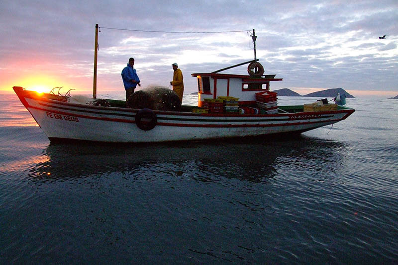 Foto de embarcação de pesca no mar, com dois pescadores.