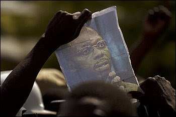 A demonstrator holds up a picture of ousted Haitian President Jean-Bertrand Aristide during a protest against Haiti's President Rene Preval in Port-au-Prince, Haiti, Monday Feb. 7, 2011. Preval's term had been scheduled to end Monday but will stay in office for three more months as his country chooses a successor in a delayed election, said his chief of staff. A group protested outside the National Palace, blocking traffic with overturned trash bins and burning tires and chanting Preval is a crook! (AP Photo/Ramon Espinosa)
