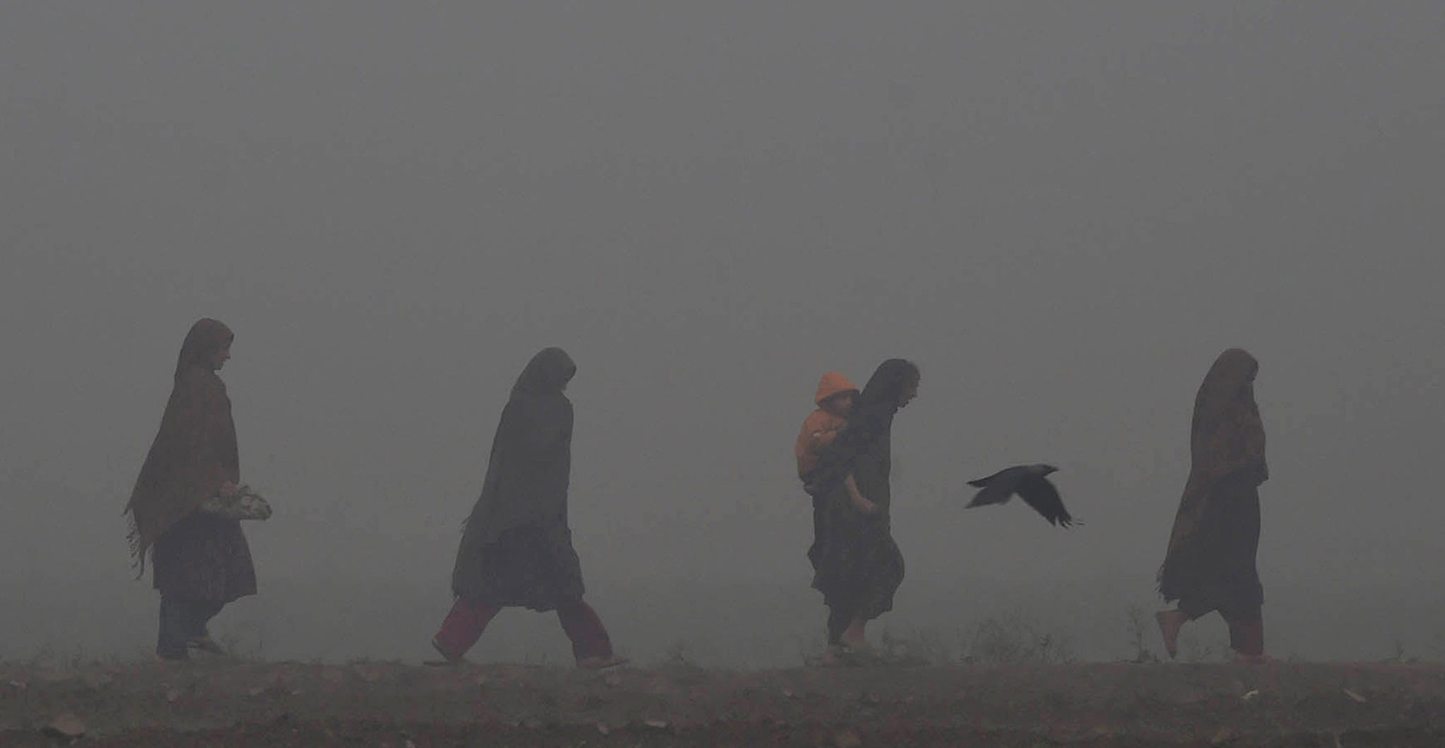 Pakistani women walk along a street on a foggy day in Lahore.