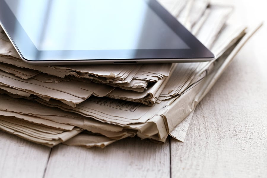 Stack of old newspapers and a tablet pc on the wooden table