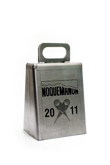 A metal cowbell with the Noquemanon logo