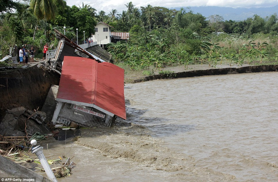 Helpless: People look on as their village hall in Iloilo province is washed into the flood waters