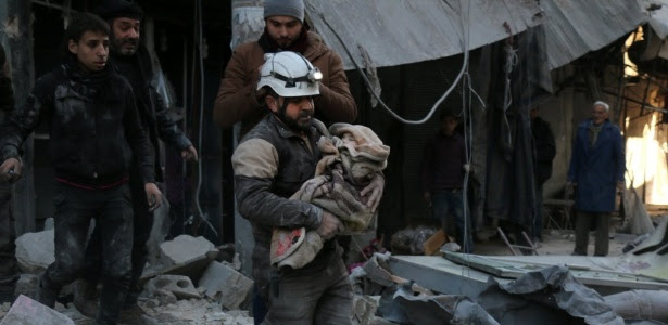 Membro da Defesa Civil síria caminha sobre escombros enquanto carrega criança envolta em um cobertor, em Aleppo, na Síria
