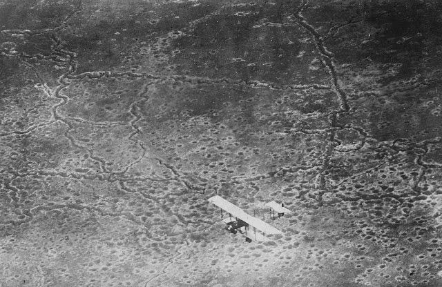 An aircraft flies over no-man's land, a European battlefield torn up by bombs and trench diggers.