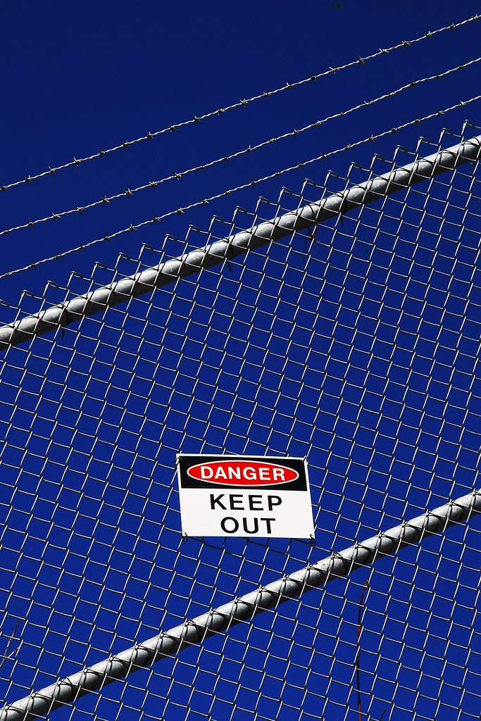 A keep out sign on a fence, with barbed wire, against a deep blue sky.