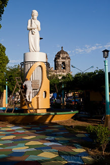 A workman paints a statue in a park in front of the Iglesia San Juan de Dios