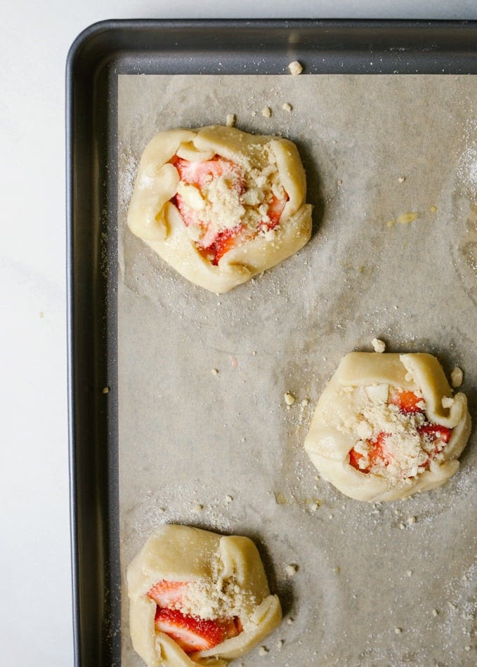 Mini Strawberry Galettes by Wood and Spoon blog. These are small open hand pies made with a simple butter dough and filled with fresh strawberries. On top an easy almond crumble adorns each dessert and a sprinkle of powdered sugar finishes them off. These little personal sized desserts are a special was to use summer produce and are sure to impress friends at parties. Find the recipe and how to on thewoodandspoon.com