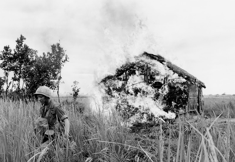 Description of  A U.S. paratrooper moves away after setting fire to house on bank of the Vaico Oriental River, 20 miles west of Saigon on Jan. 4, 1966, during a "scorched earth" operation against the Viet Cong in South Viet Nam. The 1st battalion of the 173rd airborne brigade was moving through the area, described as notorious Viet Cong territory. (AP Photo/Peter Arnett)