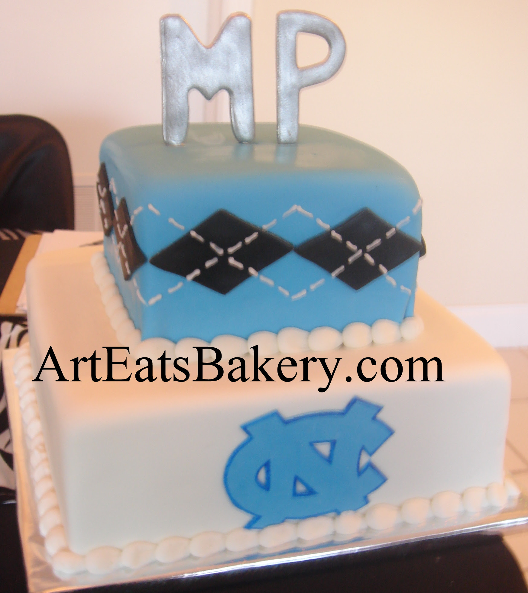 Two tier square blue, white and black men's creative custom University of North Carolina logo birthday cake design with silver monogram topper.jpg