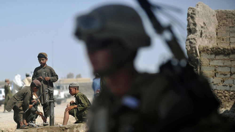 As boys washed their feet in the background, a U.S. Marine stood nearby earlier this summer in Helmand Province, Afghanistan.