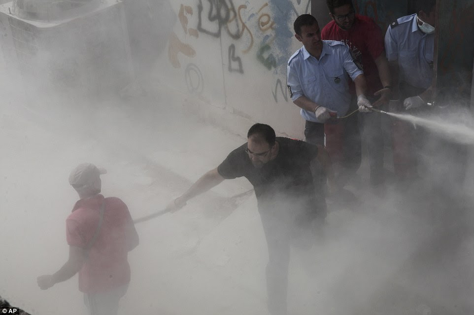 A policeman in plain clothes hits a migrant, as another sprays a fire extinguisher in an attempt to disperse hundreds of migrants