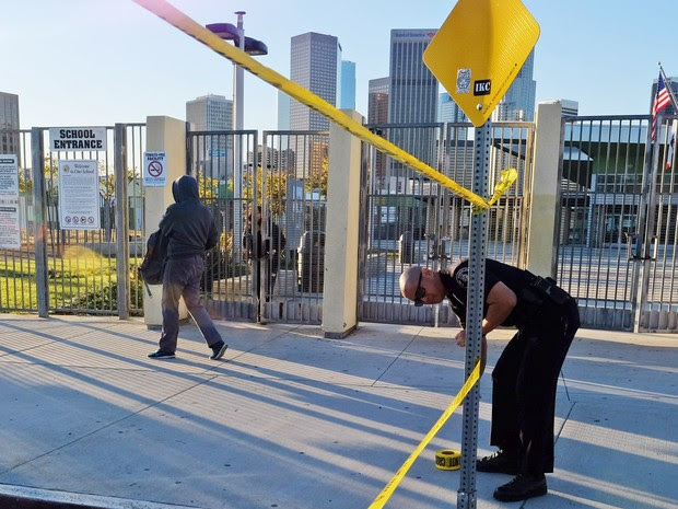 Um policial coloca fita amarela para fechar o perímetro do lado de fora da escola de ensino médio Edward Roybal em Los Angeles, nos EUA. Todas as escolsa da cidade foram fechadas nesta terça-feira (15) após uma ameaça de bomba (Foto: Richard Vogel/AP)