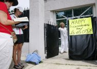 While abortion opponents pray, left, Jackson Women's Health Organization owner Diane Derzis poses at the gate of Mississippi's only abortion clinic in Jackson, Miss., Monday, July 2, 2012, after a federal judge issued a temporary restraining order Sunday, that blocked enforcement of a law that could regulate it out of business.  The law would require any physician doing abortions at the clinic to be an OB-GYN with privileges to admit patients to a local hospital. (AP Photo/Rogelio V. Solis)