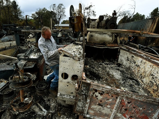 Larry Menzio examina as ruínas de sua loja de automóveis, que foi atingida por um incêndio em Middletown, na Califórnia, na quarta (16) (Foto: AFP Photo/Mark Ralston)