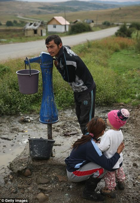Ion Varga collects water from the single community well as his relatives Claudia Gianina and Darius Varga look on