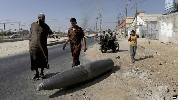 Palestinians look at an unexploded Israeli shell that landed on a road in the Gaza Strip - 1 August 2014