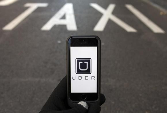 The logo of car-sharing service app Uber on a smartphone over a reserved lane for taxis in a street is seen in this photo illustration taken in Madrid on December 10, 2014. REUTERS/Sergio Perez