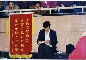'一九九四年十二月二十一日至二十九日，廣州第五期，師父在看學員心得體會，左邊是學員給師父獻上的錦旗。'