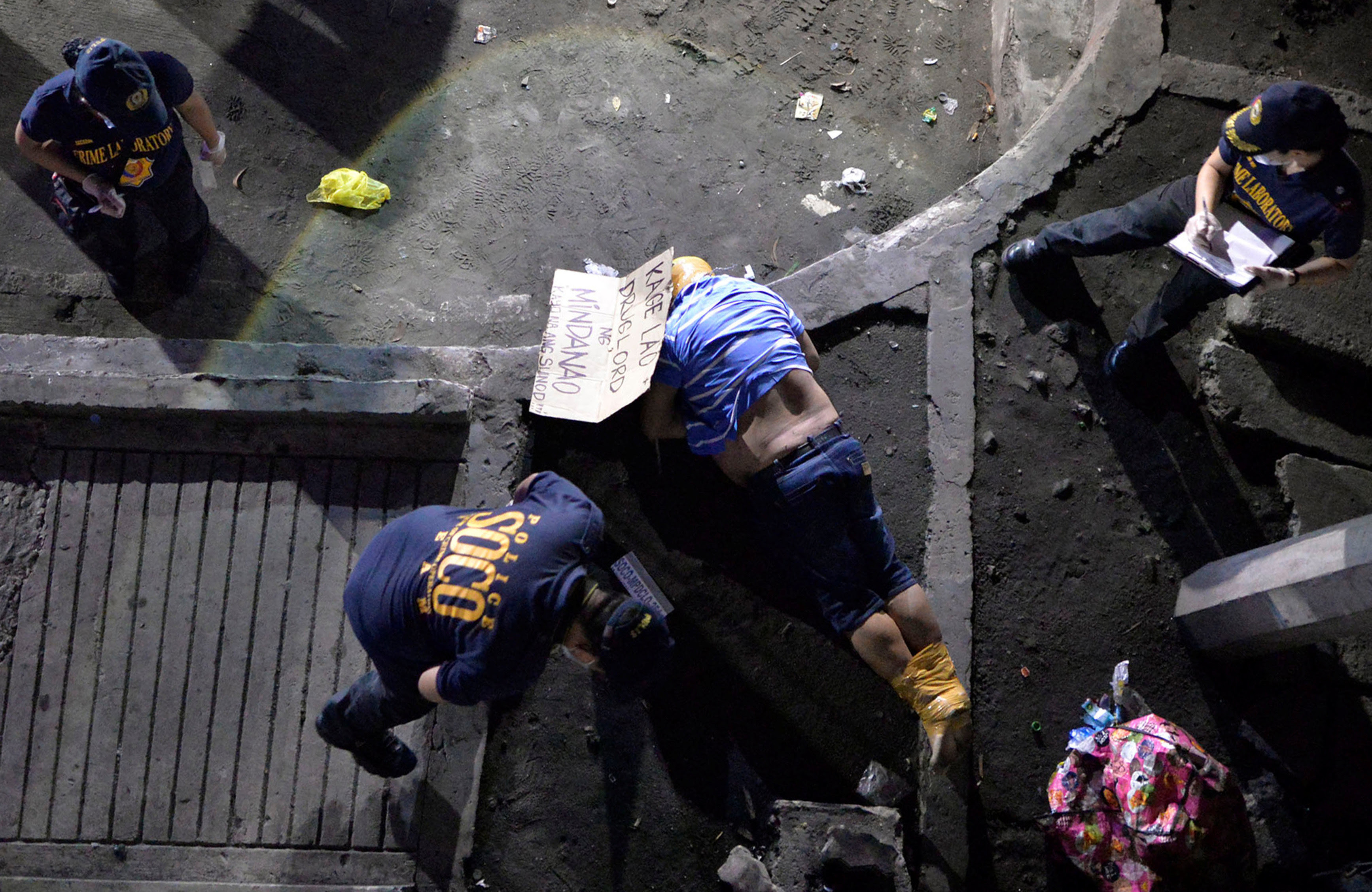 olicemen inspect the body of a man, with tape wrapped around his head and feet, who police said was a victim of drug related vigilante execution in Manila, Philippines September 21, 2016. The cardboard found near his body reads: "Kage Lao, drug lord from Mindanao. You are next".