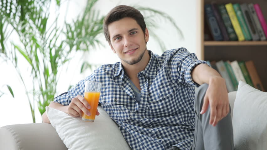 Handsome Guy Sitting On Sofa Drinking Juice And Smiling Handsome Guy Sitting On Sofa Drinking Juice And Smiling