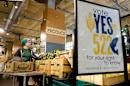 File photo of an employee stocking produce near a sign supporting a ballot initiative that would require labeling of foods containing genetically modified crops at the Central Co-op in Seattle