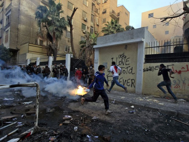 Manifestante carrega gás lacrimogêneo durante confrontos com a polícia perto da Praça Tahrir (Foto: AP)