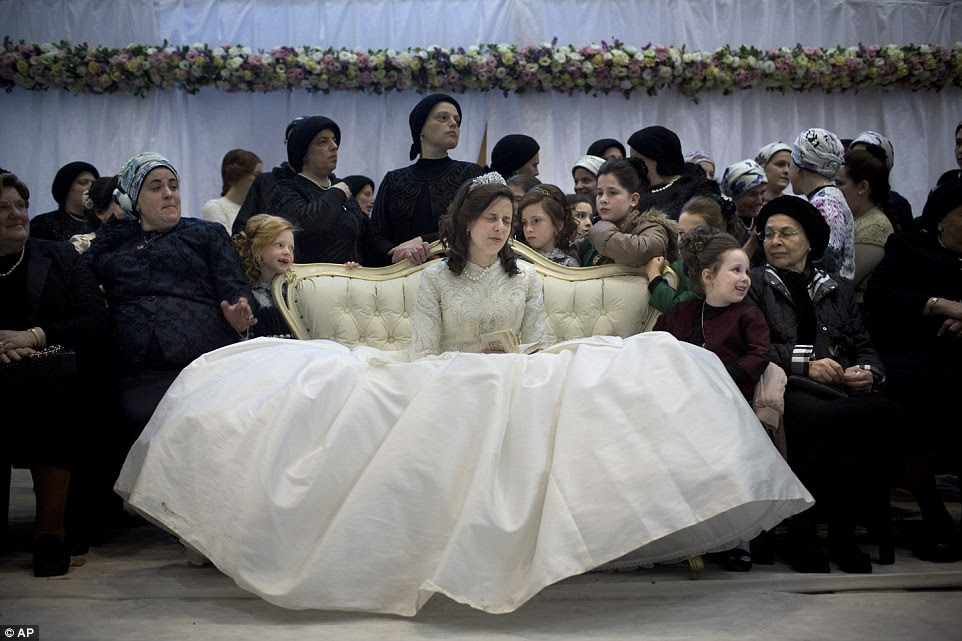 Guests share a joke as the bride closes her eyes in prayer, her dress spread out around her