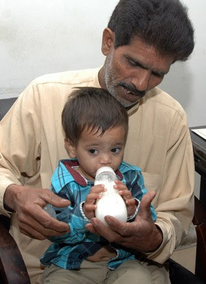 Muhammad Yasin segura o neto de apenas 9 meses enquanto ele toma uma mamadeira no escritório de advocacia (Foto: AFP)
