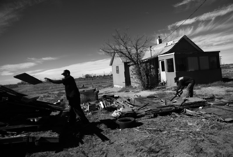 Description of  SUGAR CITY, CO - NOVEMBER 04: Nathan Vaisa, left, and Harry Tomlin clean up around an abandoned home in Sugar City, November 04, 2013. The two work for a local bank that will try to auction off the property.