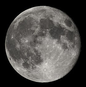 Moon just past full, in the darkness of the night sky. It is patterned with a mix of light-tone regions and darker, irregular blotches, and scattered with varying sizes of impact craters, circles surrounded by out-thrown rays of bright ejecta.