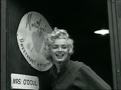 Marilyn Monroe waves to US troops in front of door sign saying, "Marilyn - Sweetheart of the Bayonet Division", during entertainment tour, Korea; Feb 54