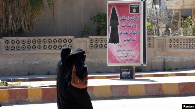 Veiled women walk past a billboard that carries a verse from Koran urging women to wear a hijab in the northern province of Raqqa March 31, 2014.