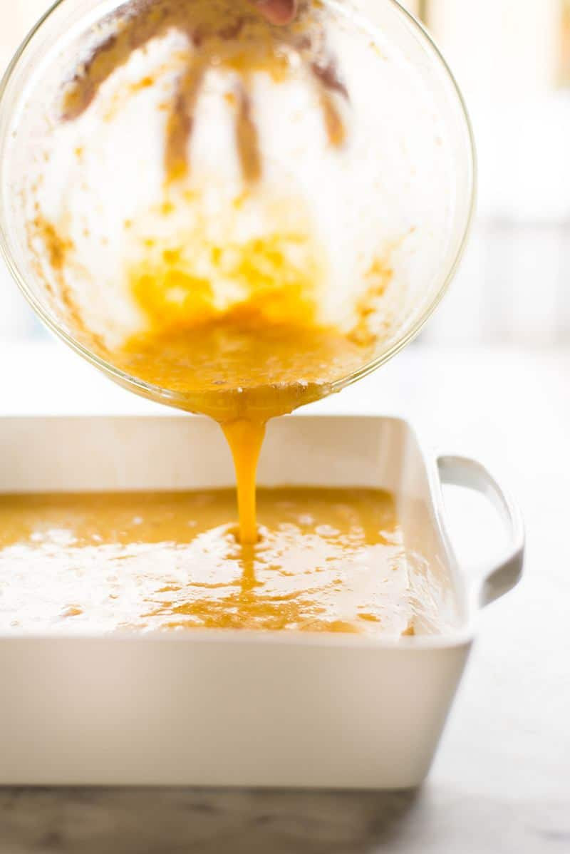 Image of pouring the lemon filling of the lemon bars onto the spelt flour crust. This will then be transferred to the oven and baked.