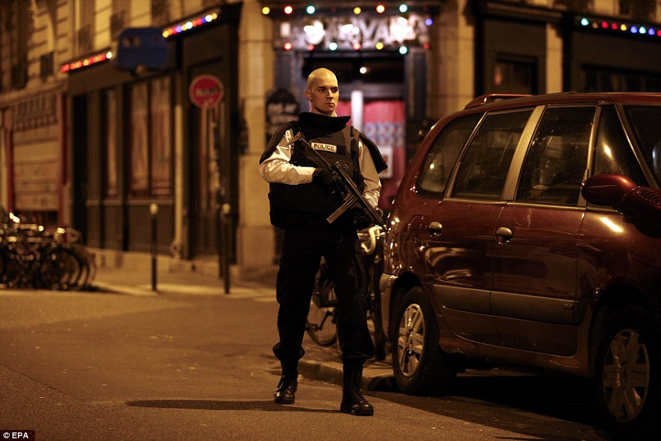 On guard: A machine gun-wielding police officer stands to attention on a street near the scene of the restaurant shooting