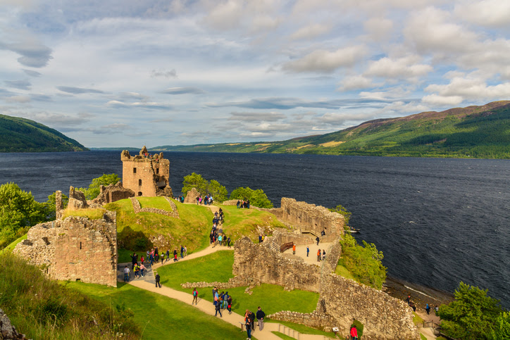 Inverness, Scotland  - August 10, 2017: View of Urquhart Castle in Scotland with a row of visitors exploring castle ruins.