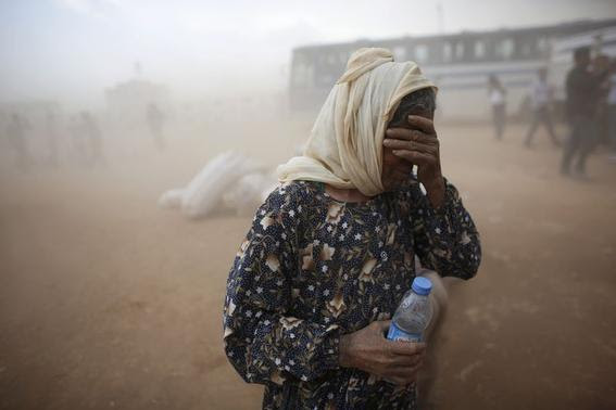A Kurdish Syrian refugee covers her face as she waits for transport during a sand storm on the Turkish-Syrian border near the southeastern town of Suruc in Sanliurfa province, September 24, 2014.     REUTERS-Murad Sezer