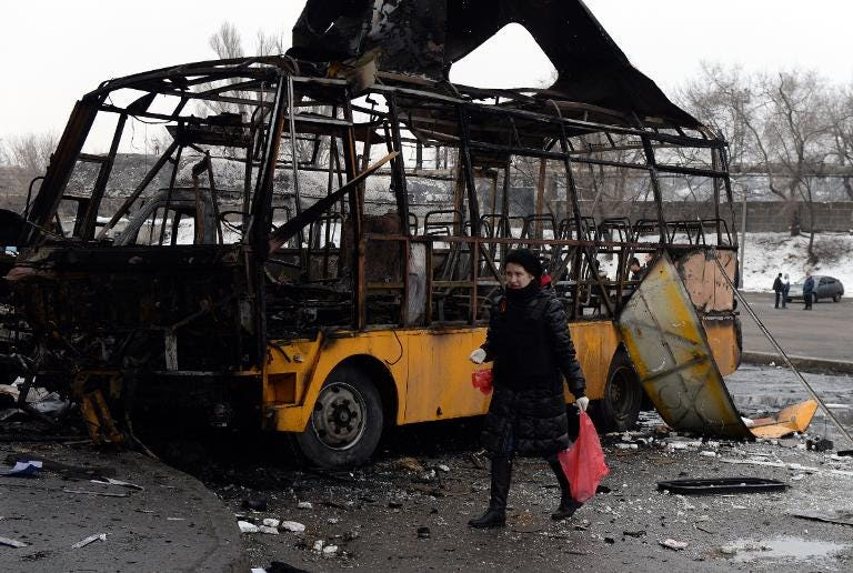 A woman walks past a destroyed bus in Donetsk on February 11, 2015