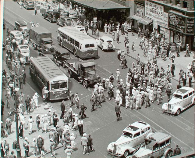 Herald Square, 34th and Broadway, Manhattan. Looking down on busy intersection, people crossing, buses, trucks, cabs, other autos, Macy's entrance just visible with union picket in front.